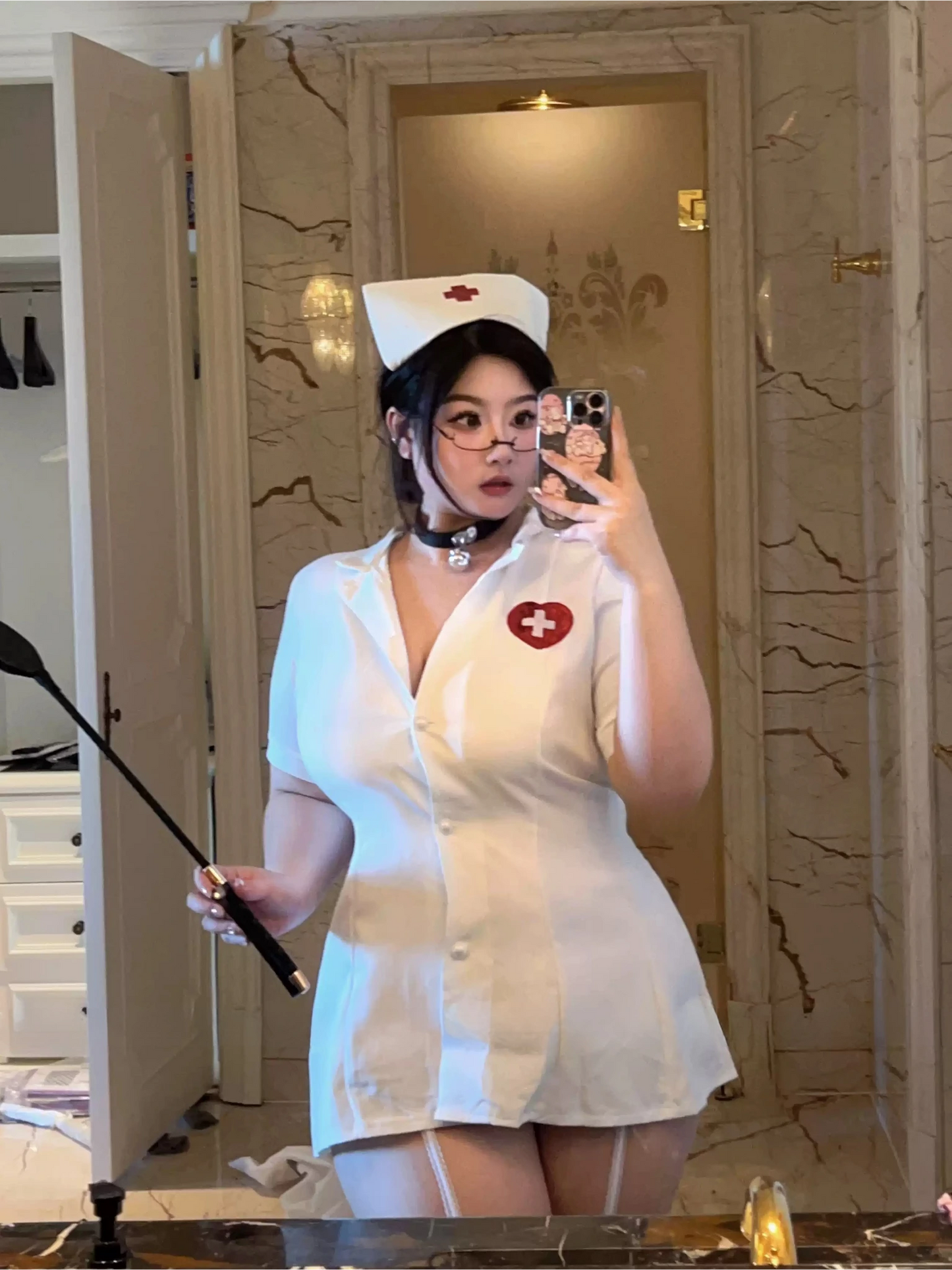 Close-up of a white nurse cosplay outfit featuring a red cross heart badge and riding crop accessory.